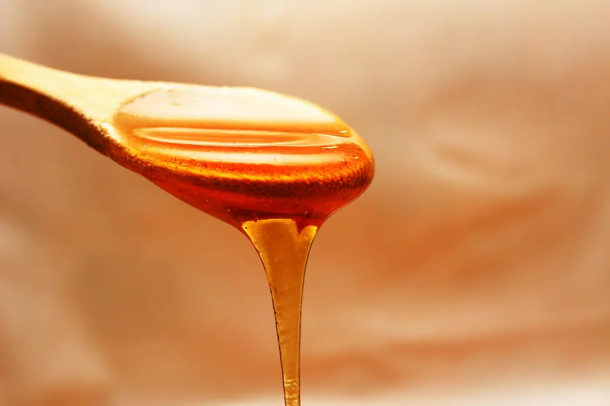 Honey being drizzled from a wooden dipper